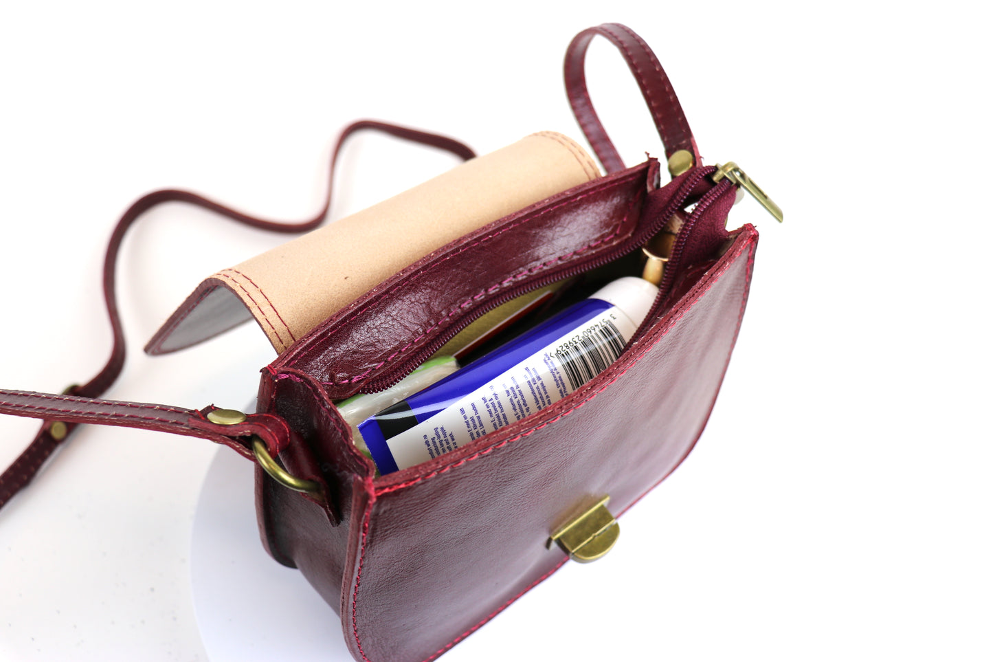 Open view of the dark Red Cora Vintage Small Leather Crossbody Bag showing its interior space, with visible contents such as a wallet and phone.