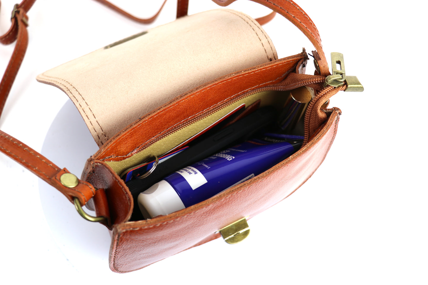 Open view of the light tan Cora Vintage Small Leather Crossbody Bag, filled with items like a phone and wallet, on a white background.