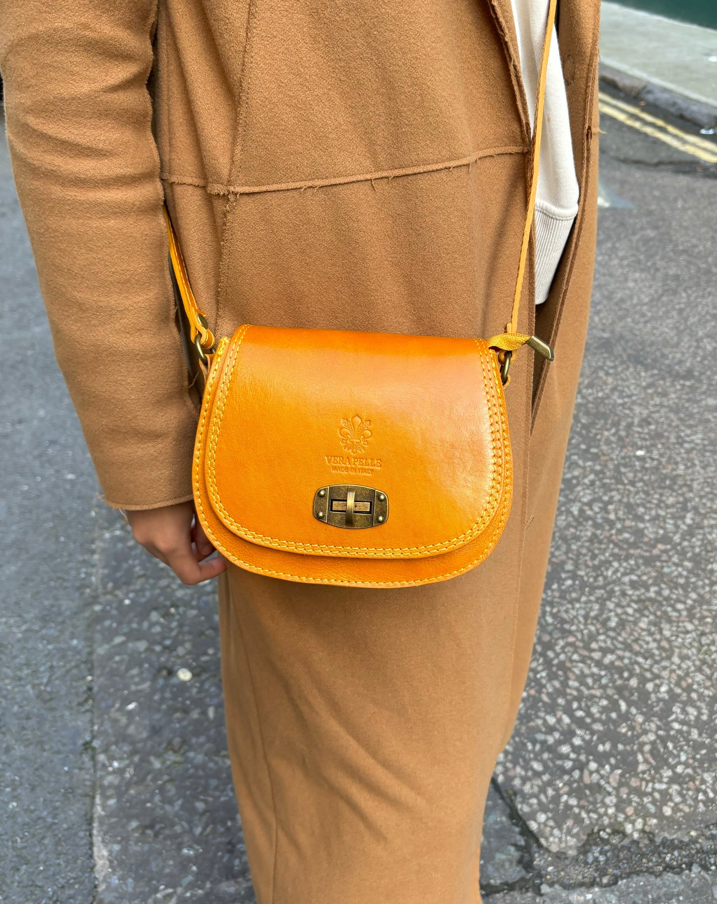 A model wearing the mustard yellow Cora Vintage Small Leather Crossbody Bag paired with a beige coat, styled for a street look.
