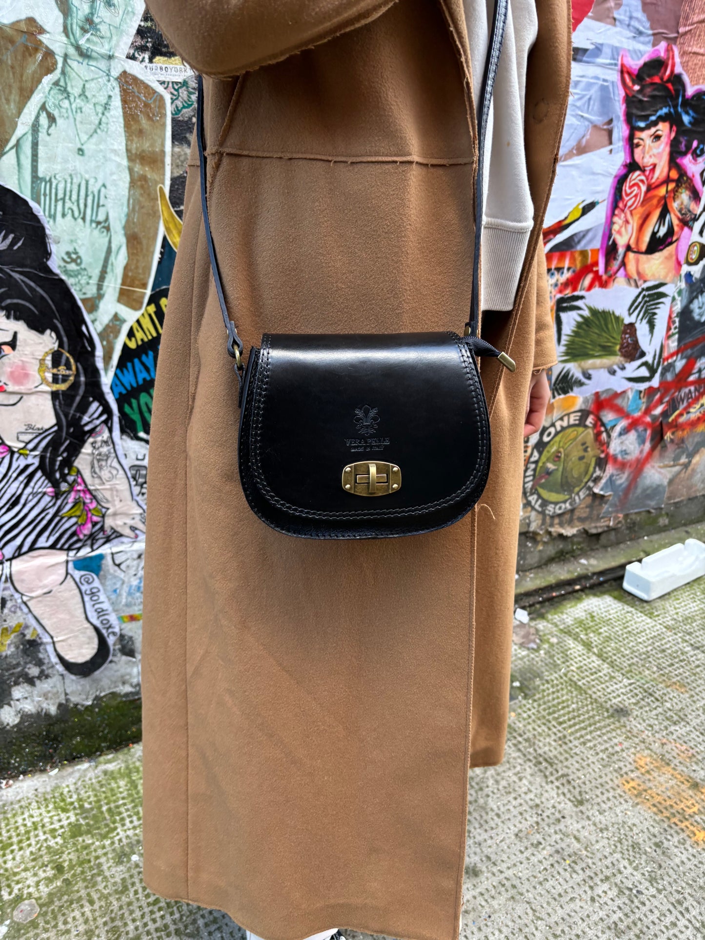 A model wearing a black Cora Vintage Small Leather Crossbody Bag paired with a beige coat for a street-style look.