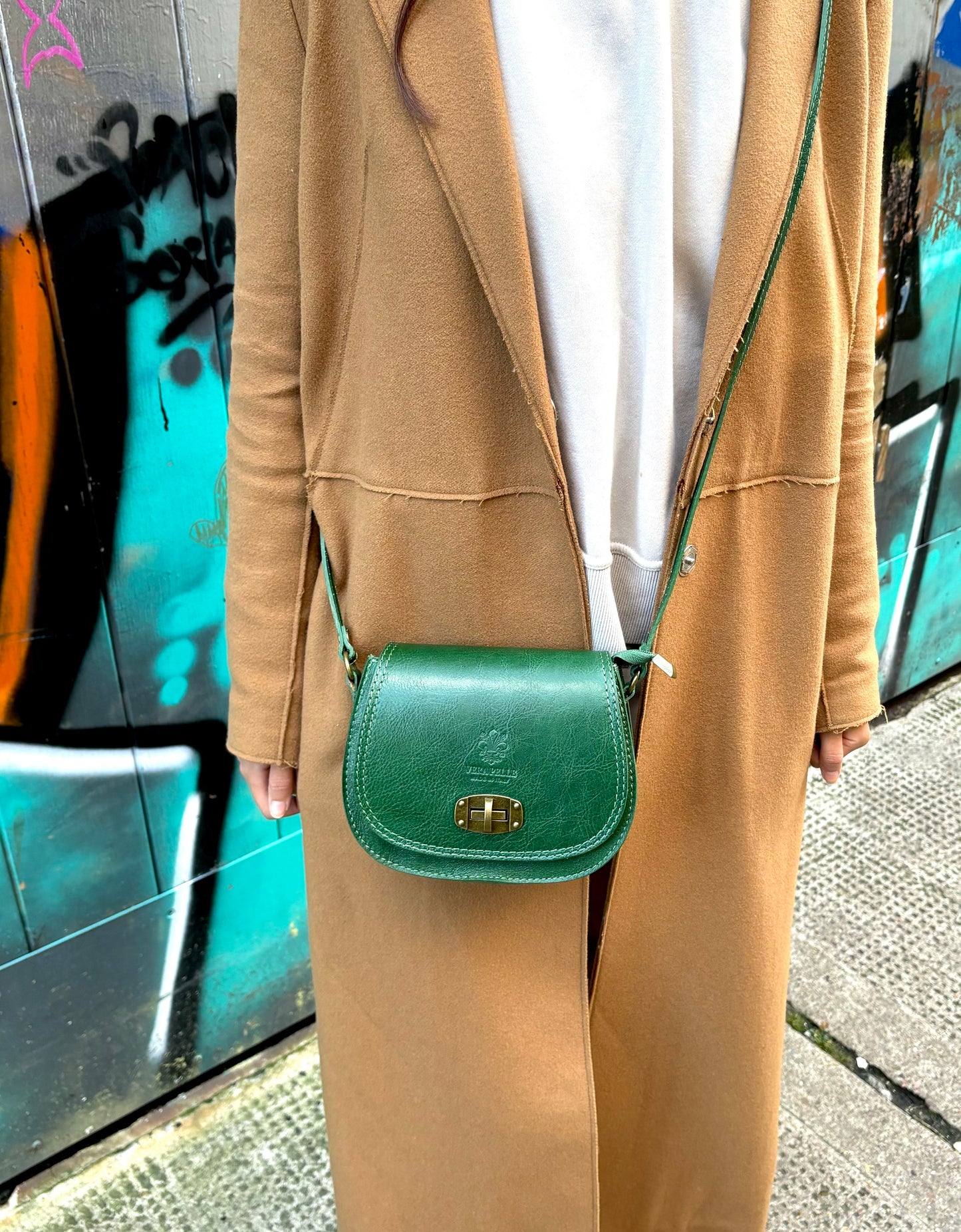 A model wearing a green Cora Vintage Small Leather Crossbody Bag, paired with a beige coat, showcasing a street-style look.