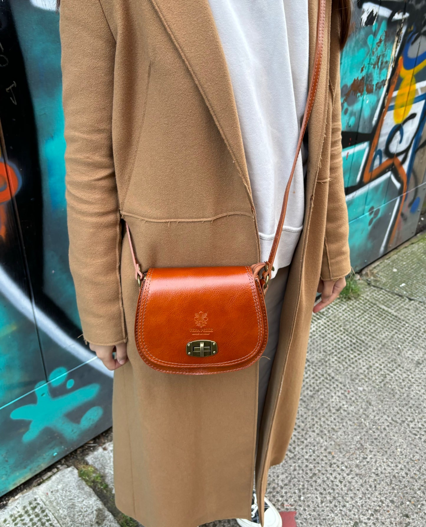 A model wearing a light tan Cora Vintage Small Leather Crossbody Bag paired with a beige coat for a casual street-style look.