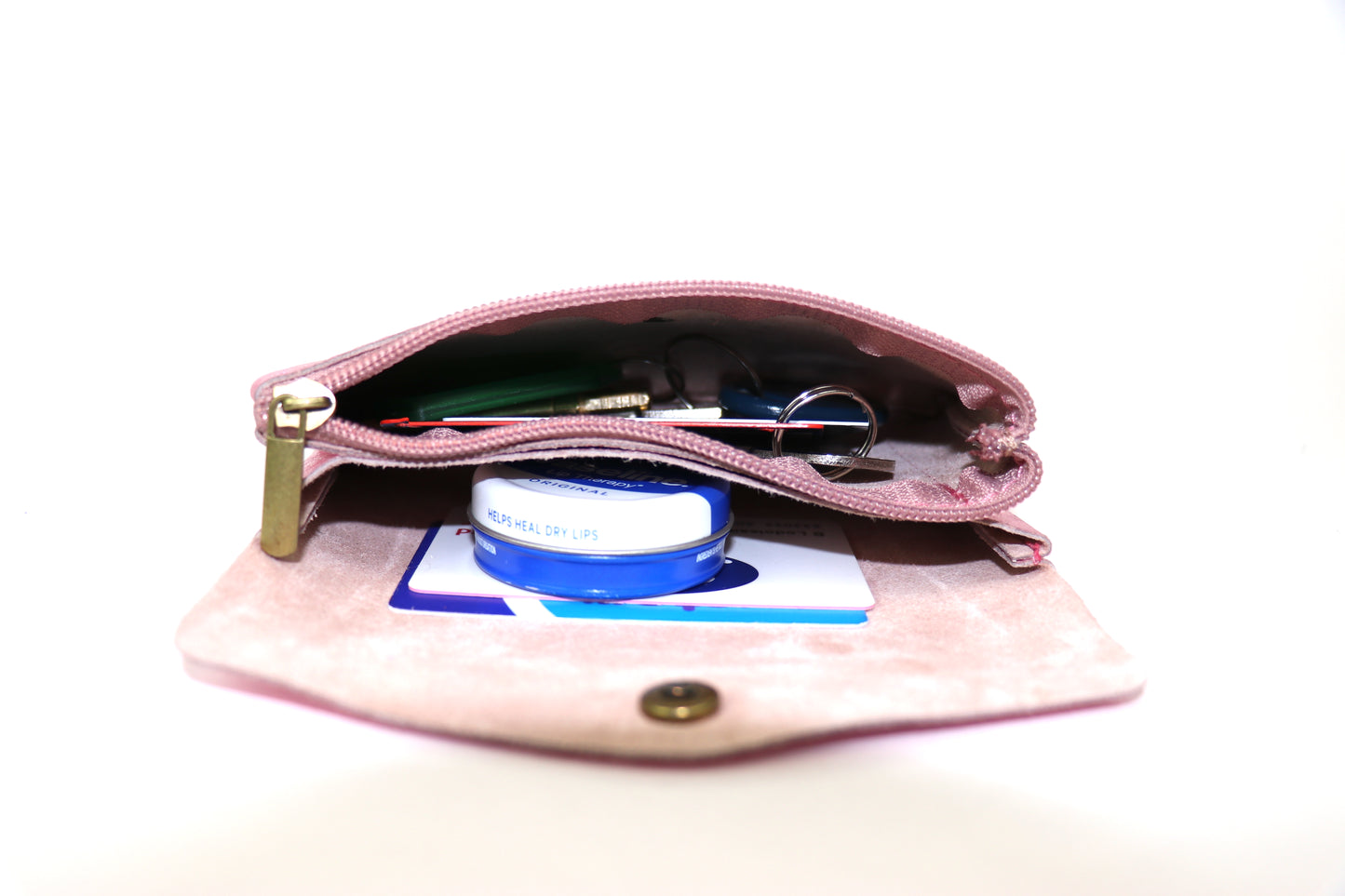 A light pink metallic pouch is opened, displaying its interior filled with small items like lip balm, keys, and cards. The pouch is shown from a low-angle view, highlighting the spaciousness and functionality of the interior compartments.