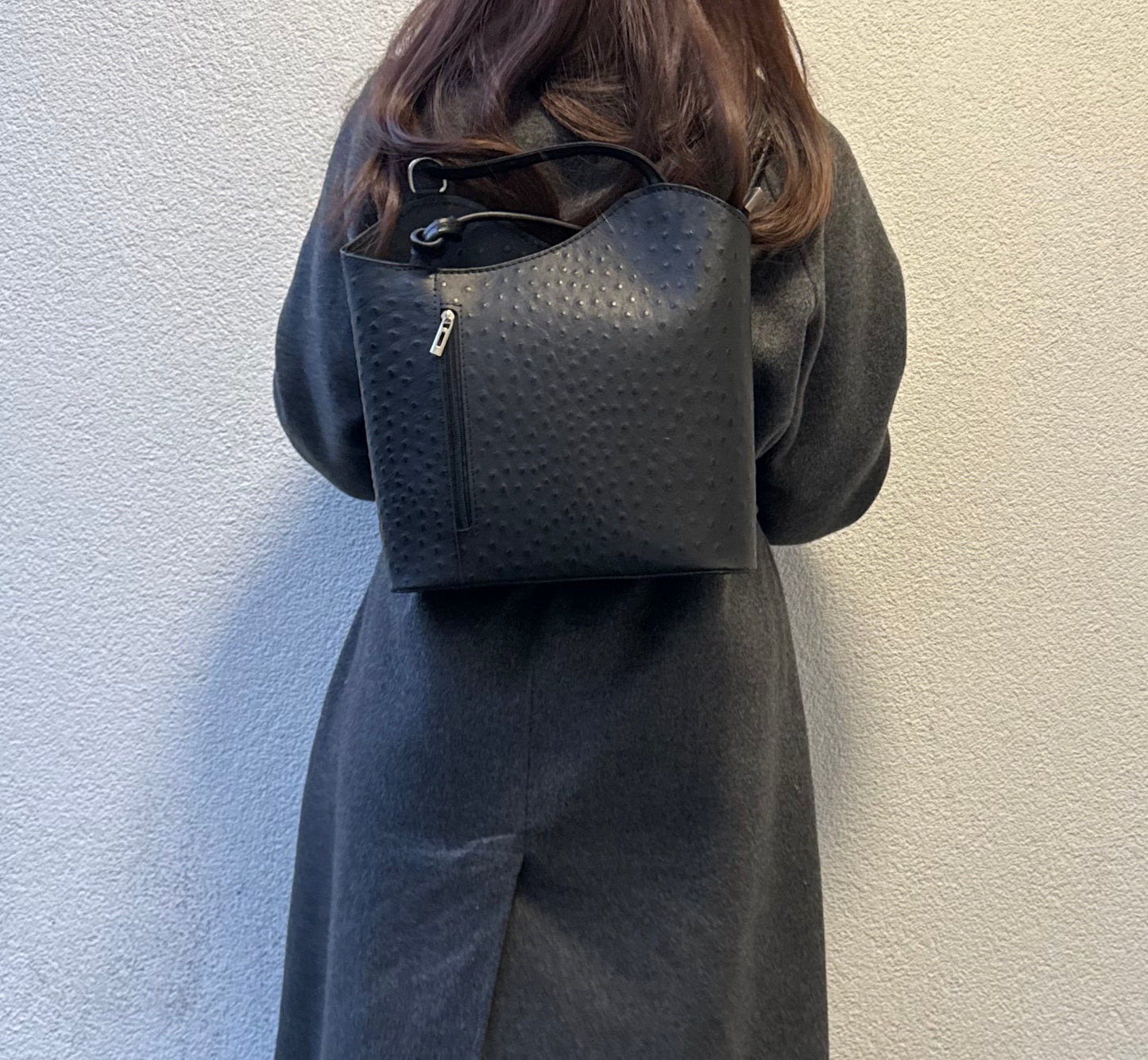 Woman wearing a Black Single-Tone Ostrich Style Italian Leather Convertible Backpack, full back view highlighting the style.