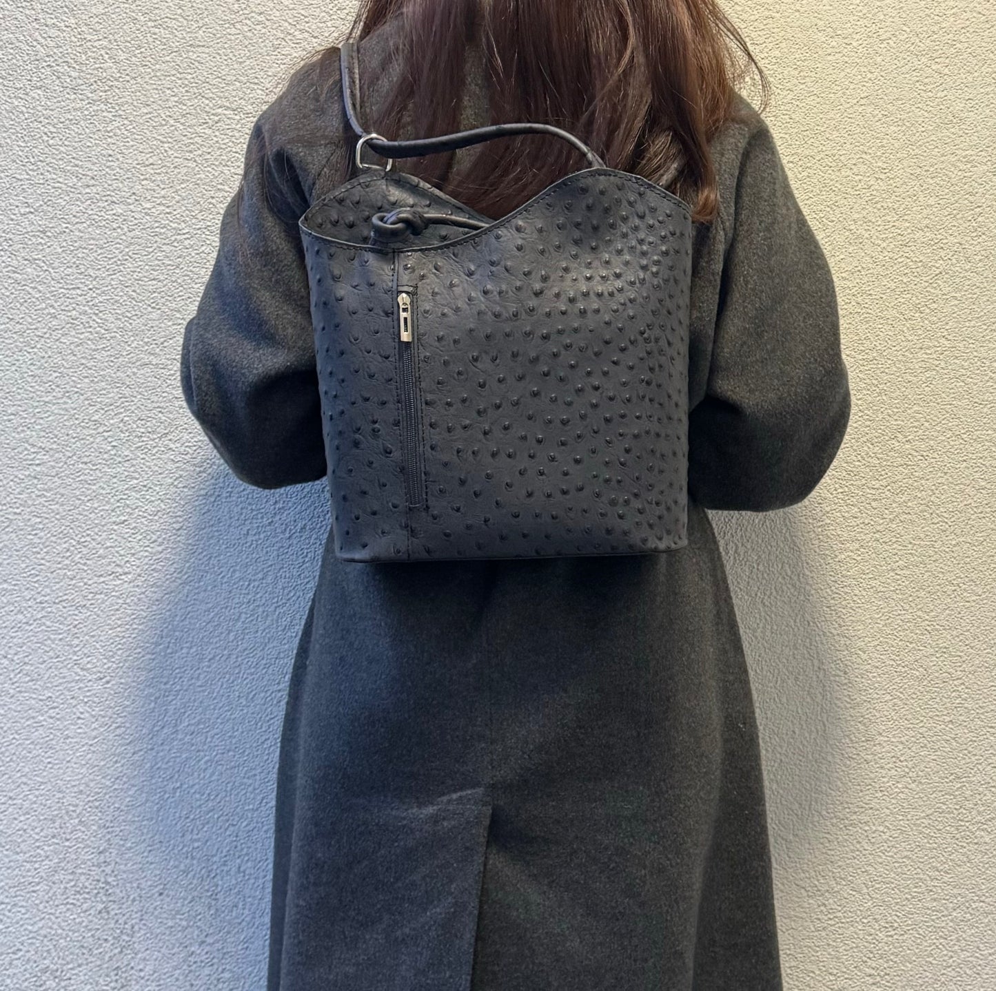 Woman wearing a grey Single-Tone Ostrich Style Italian Leather Convertible Backpack, full back view showcasing the versatility of the bag.