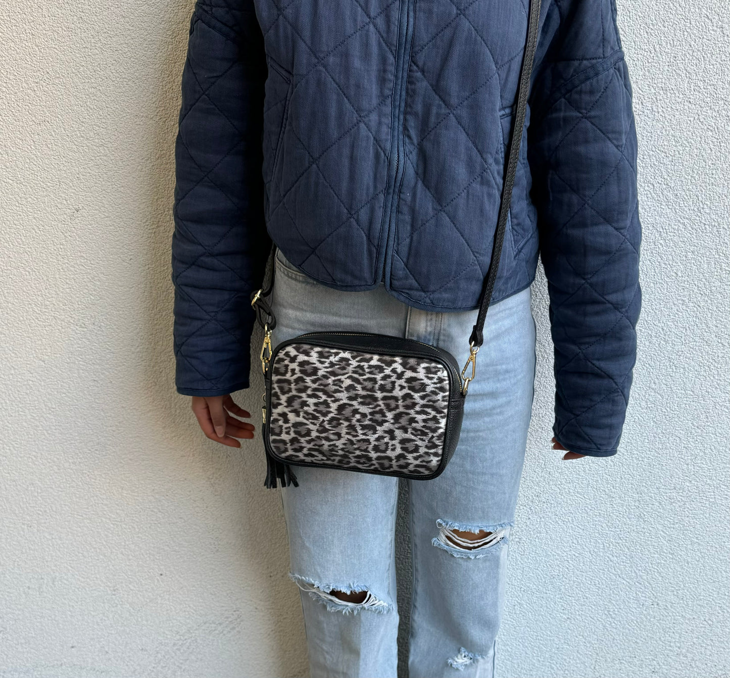 Person wearing a Leather Leopard print bag crossbody style, paired with casual jeans and a jacket.
