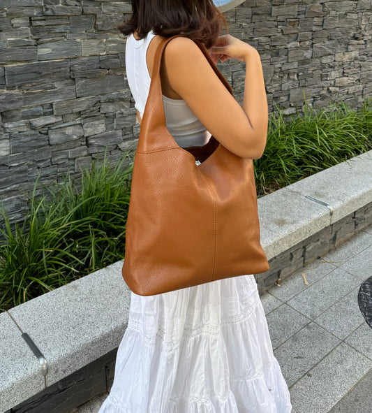 Woman carrying a large brown leather tote bag over her shoulder outdoors.