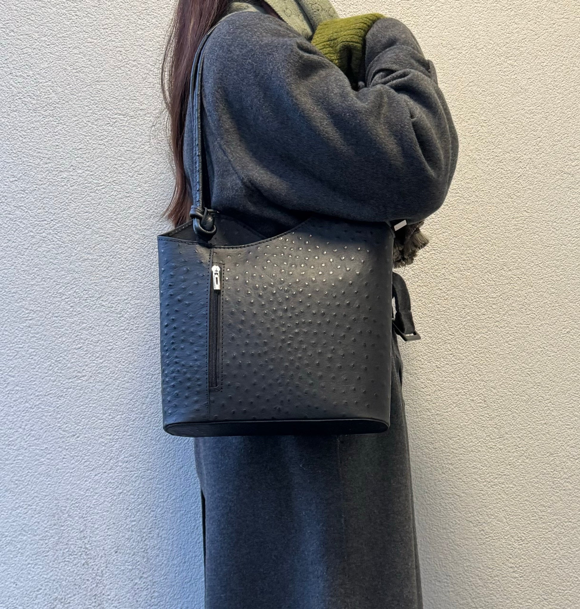 Woman wearing a Black Single-Tone Ostrich Style Italian Leather Convertible Backpack, angled side view highlighting the structured design.
