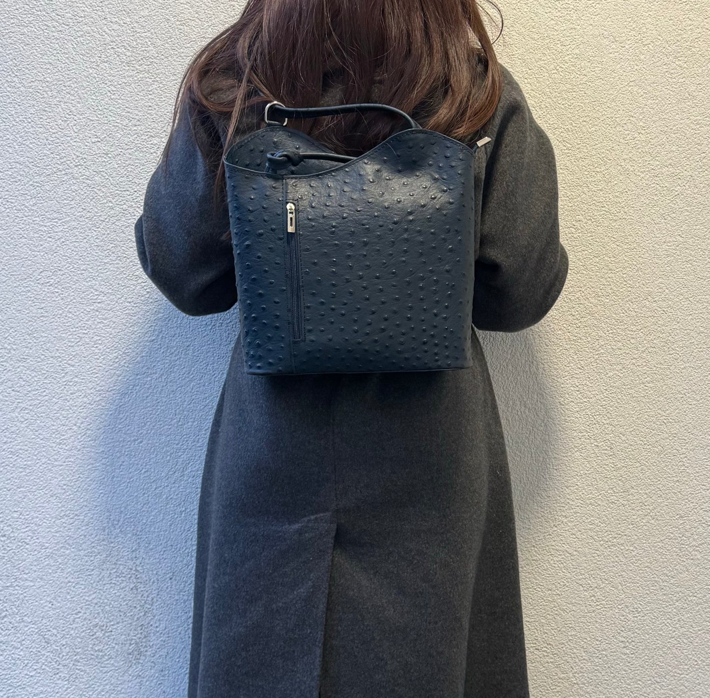 Woman wearing a navy Single-Tone Ostrich Style Italian Leather Convertible Backpack, full back view highlighting the chic green design.
