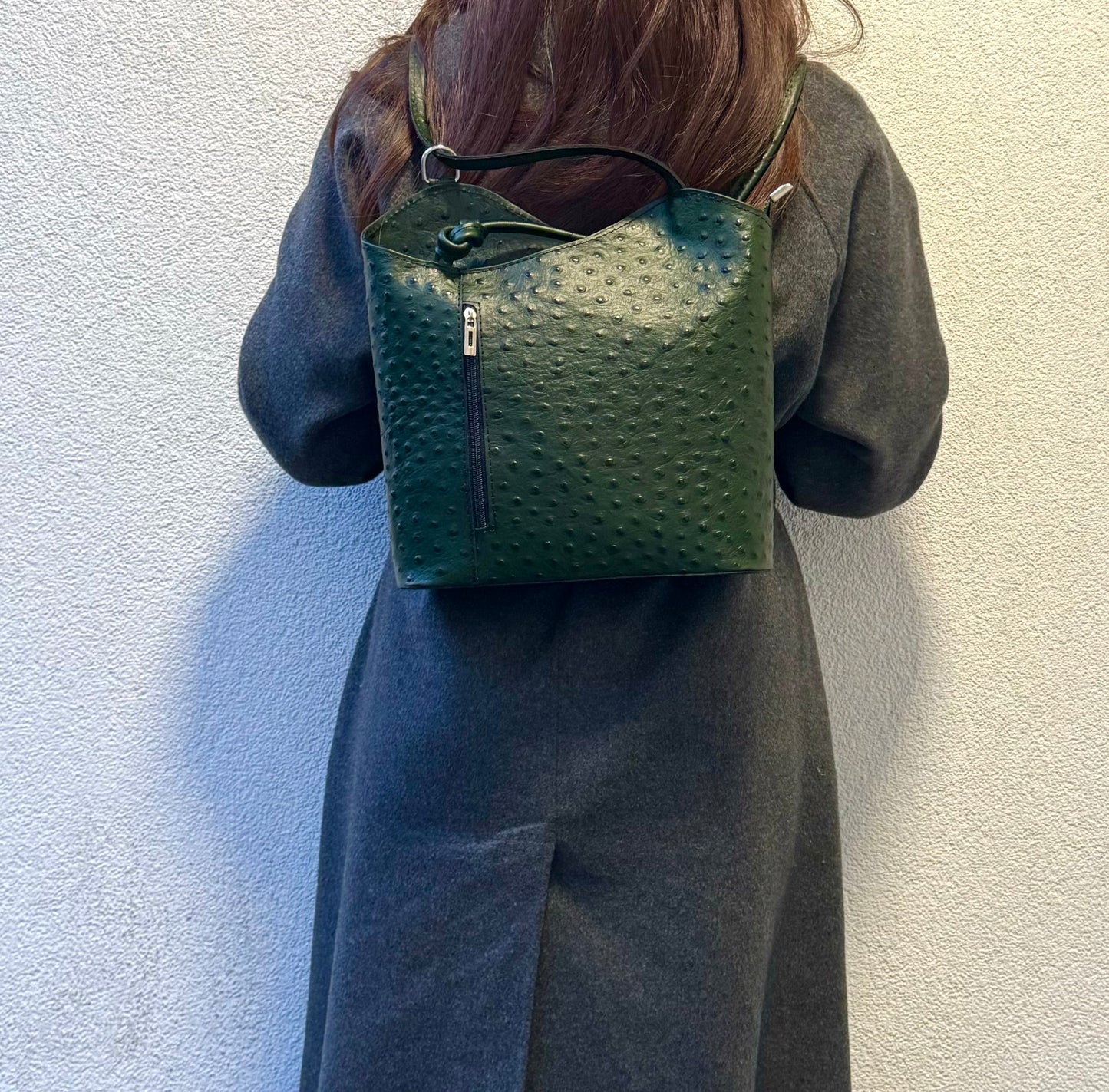 Woman wearing a Green Single-Tone Ostrich Style Italian Leather Convertible Backpack, back view highlighting the deep green shade.
