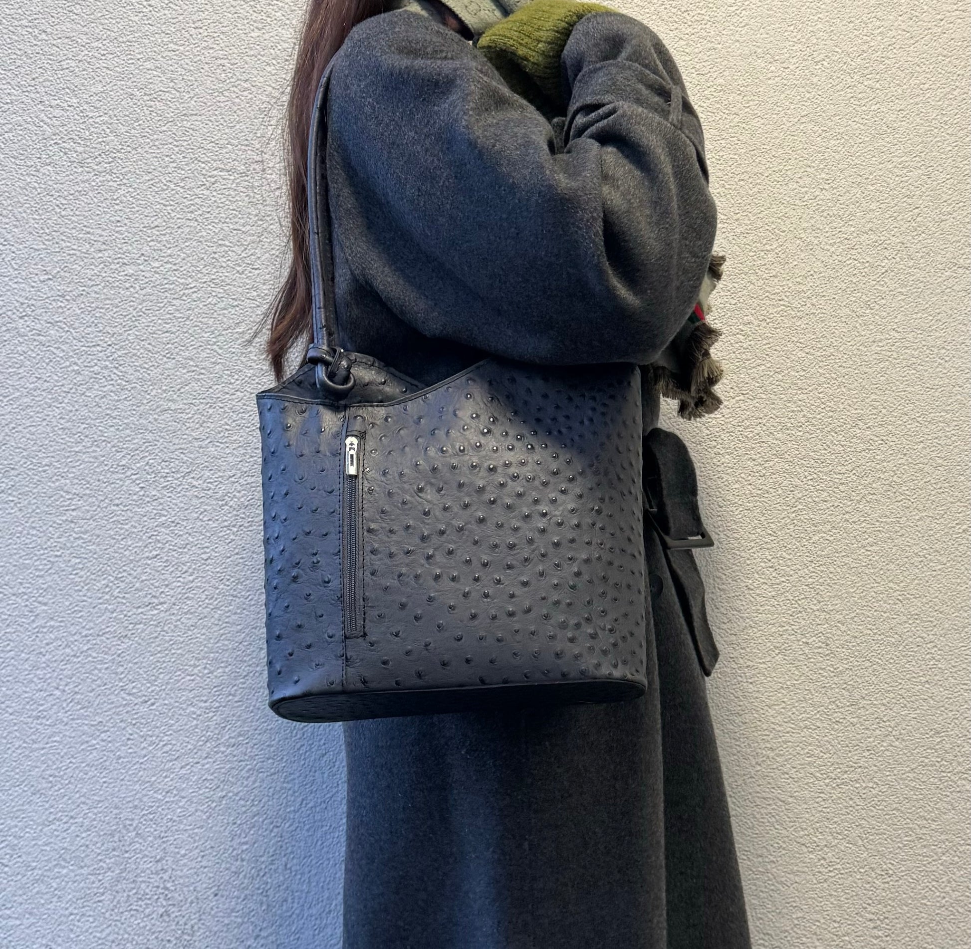 Woman wearing a grey Single-Tone Ostrich Style Italian Leather Convertible Backpack, angled side view highlighting the structured design.
