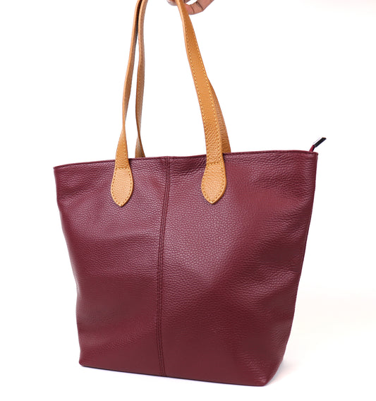 Berry leather tote bag with tan leather handles, displayed in a front view. The bag is being held by one handle, showing its structured design and pebble-grain texture.