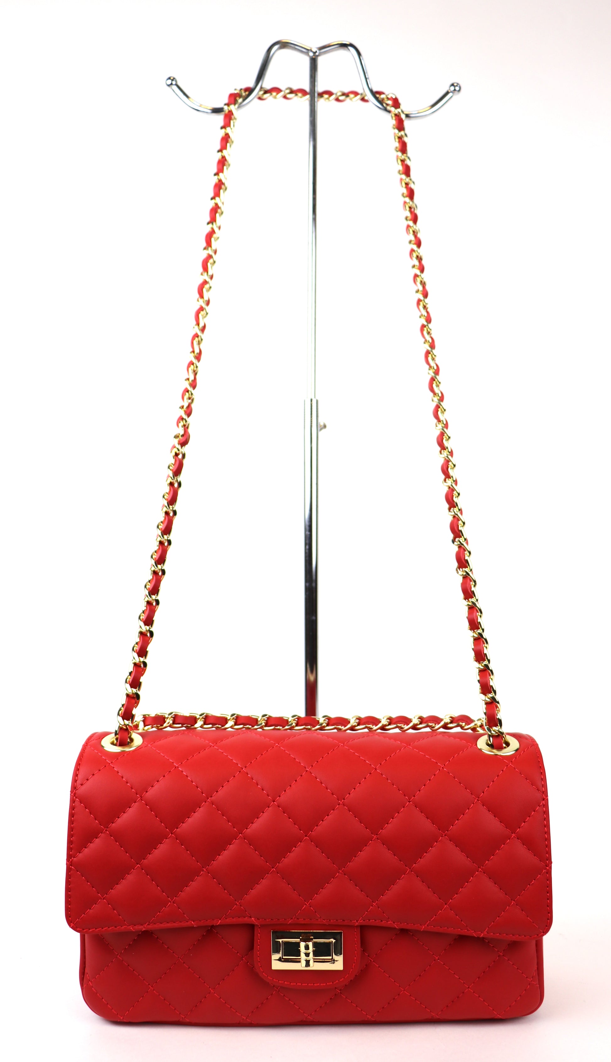 A vibrant red quilted leather bag displayed on a metal stand, featuring a gold twist-lock closure and a red and gold chain strap. The bag's bold color and classic quilted pattern create a striking, fashionable look.