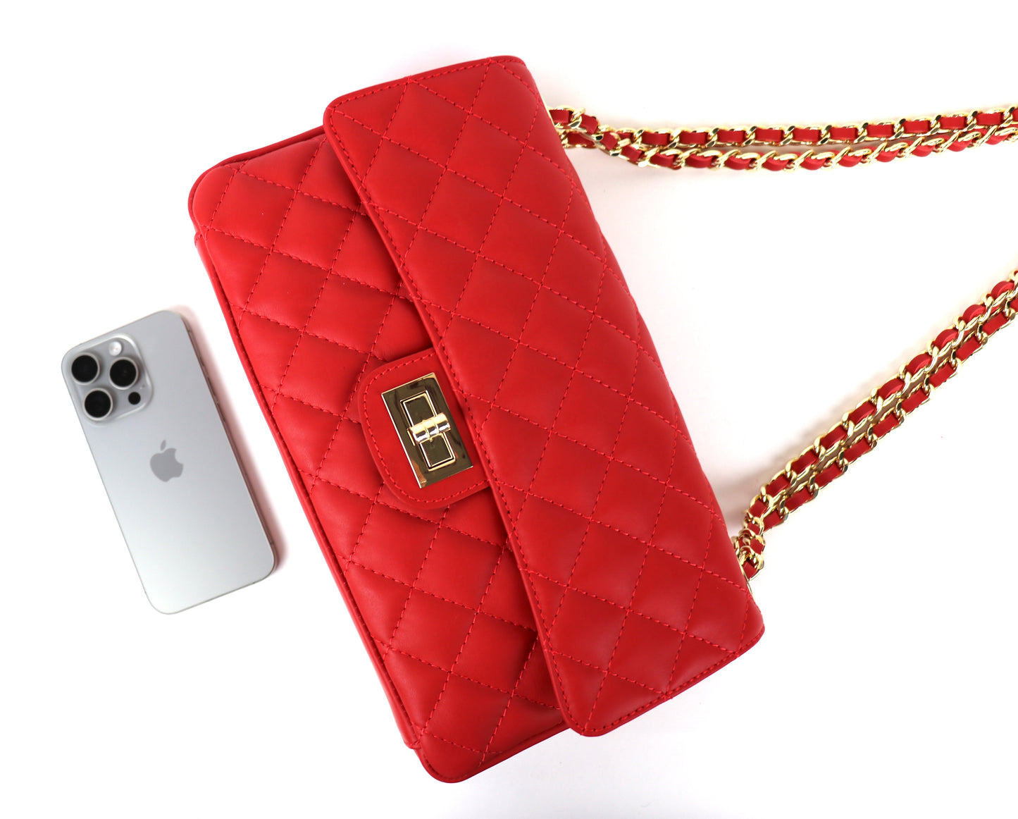 A side view of the red quilted bag, placed next to a smartphone for size reference.
