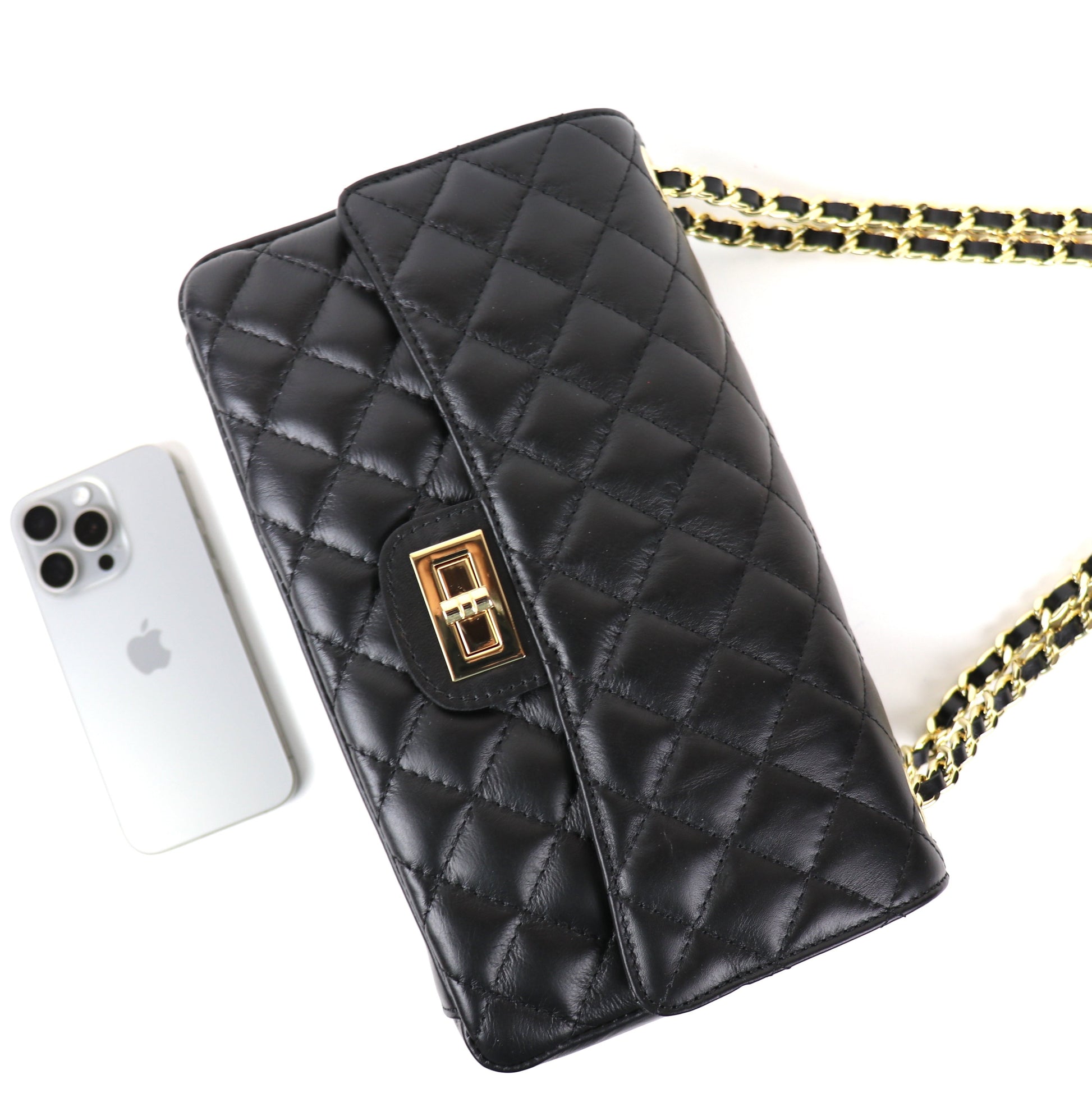 A black quilted leather bag with a gold twist-lock closure, shown next to a silver iPhone for size reference. The bag features a black and gold chain strap, highlighting its sleek and elegant design.