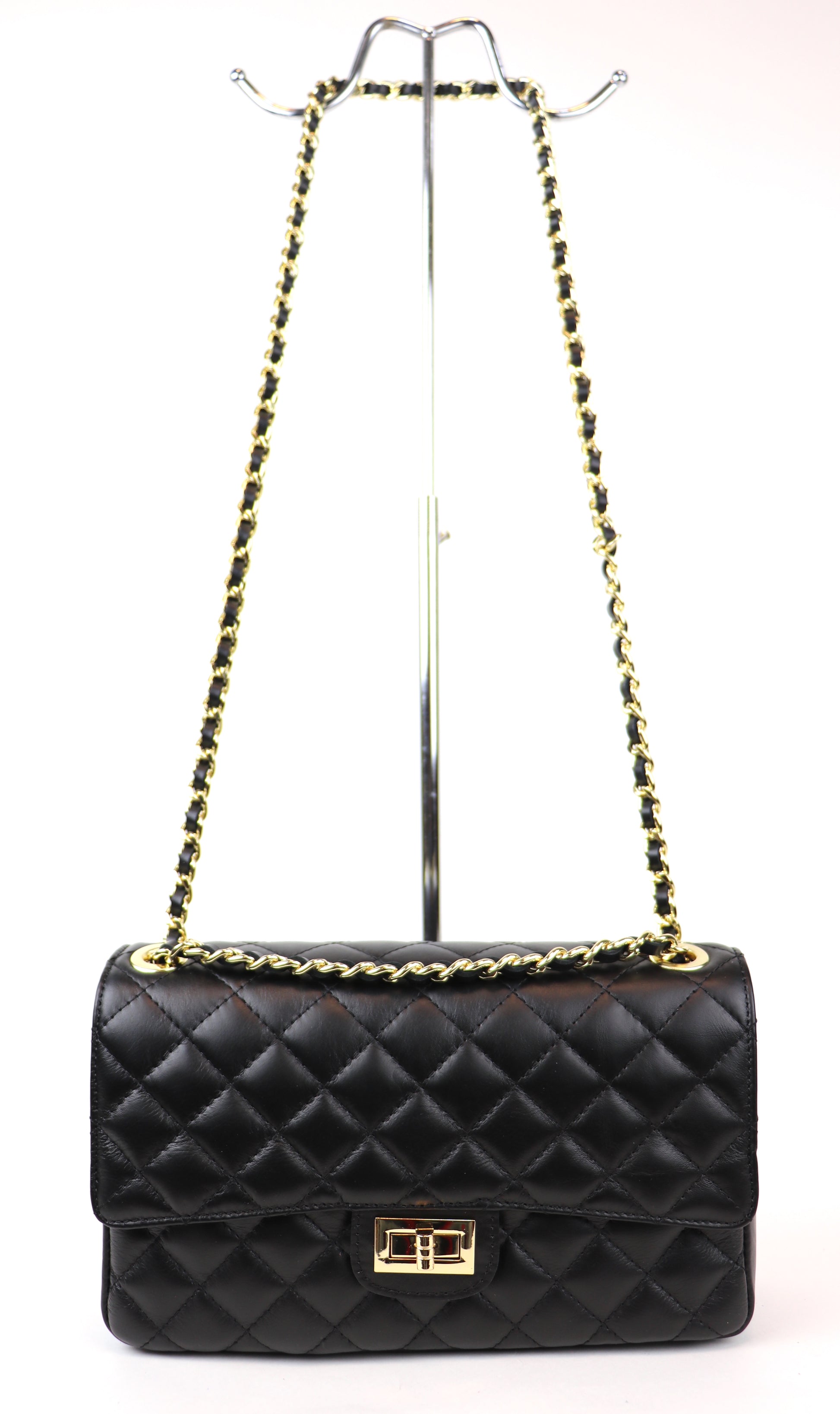 A black quilted leather bag displayed on a metal stand, featuring a gold twist-lock closure and a black and gold chain strap. The bag's structured design and classic quilted pattern give it an elegant and timeless appearance.