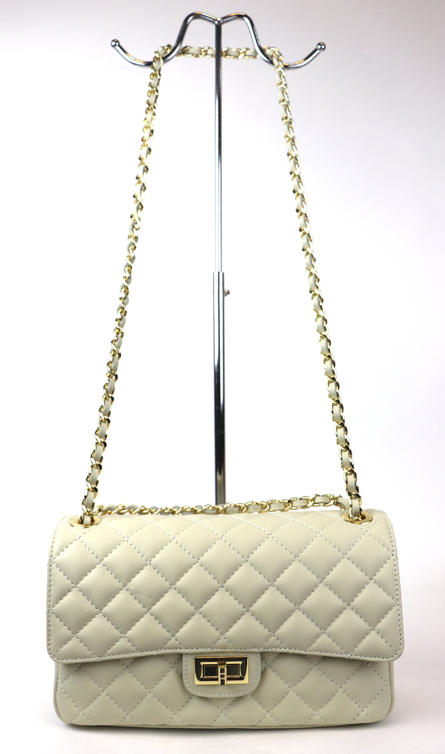 A cream-colored quilted leather bag with a gold twist-lock closure and chain strap, displayed on a metal stand against a plain background.






