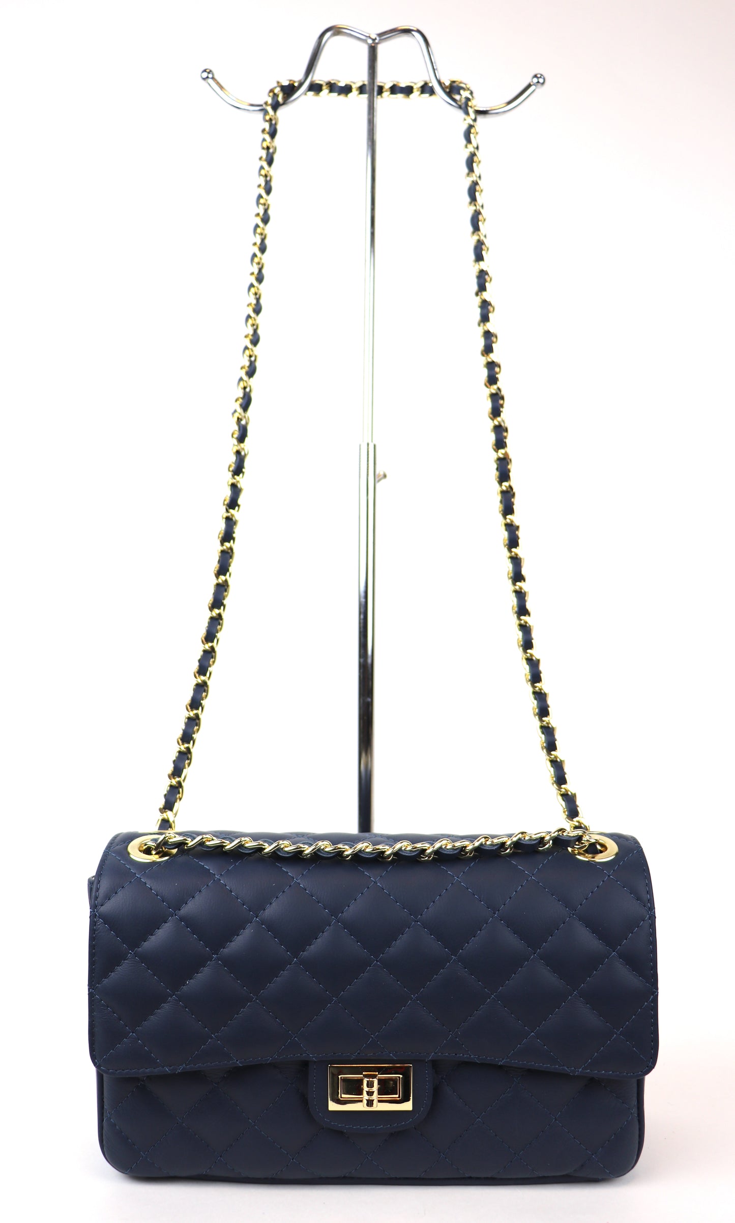 A navy blue quilted leather bag with a gold twist-lock closure and black-and-gold chain strap, displayed on a metal stand.









