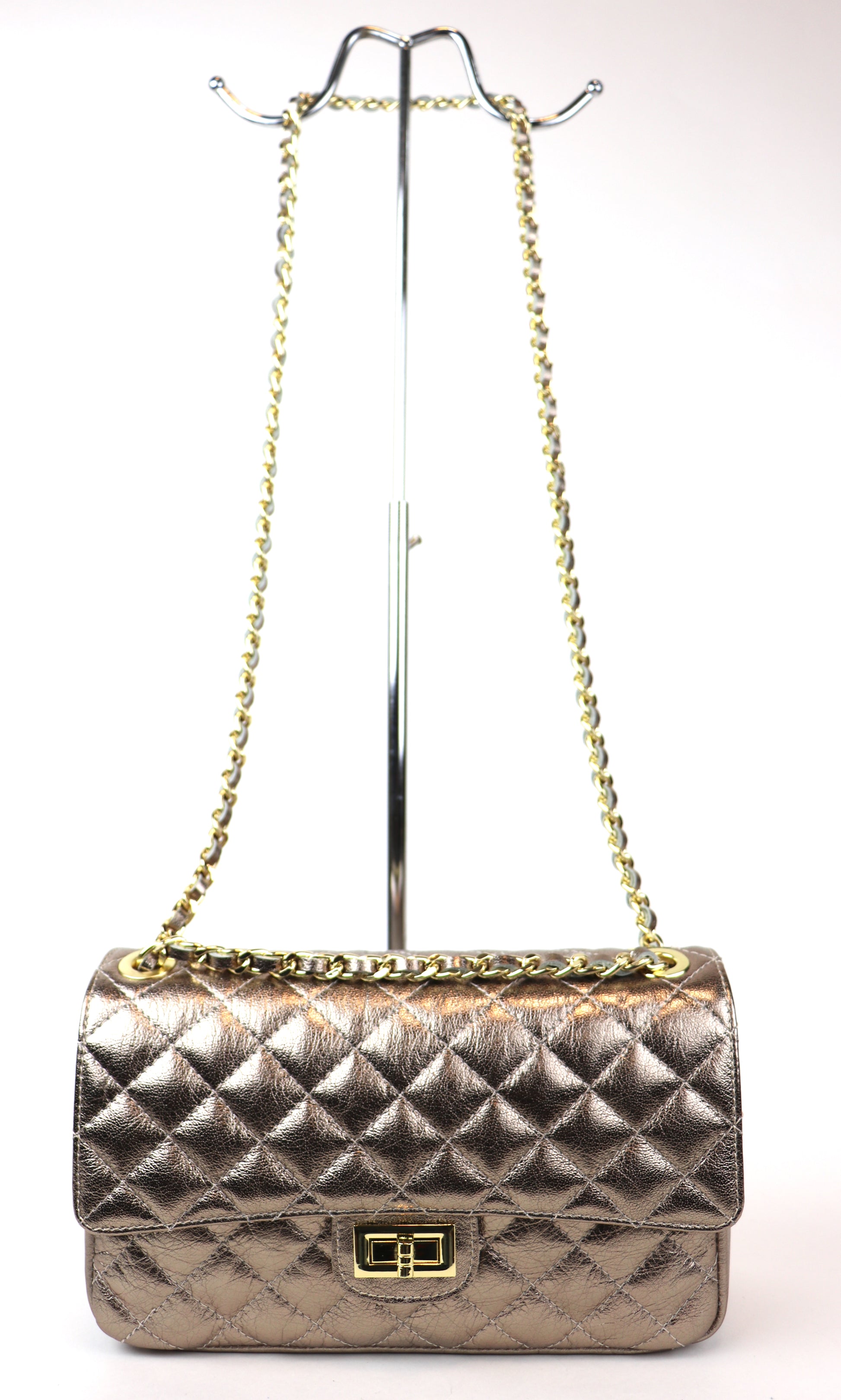 A bronze quilted leather bag with a gold chain strap and twist-lock closure displayed on a metal stand.