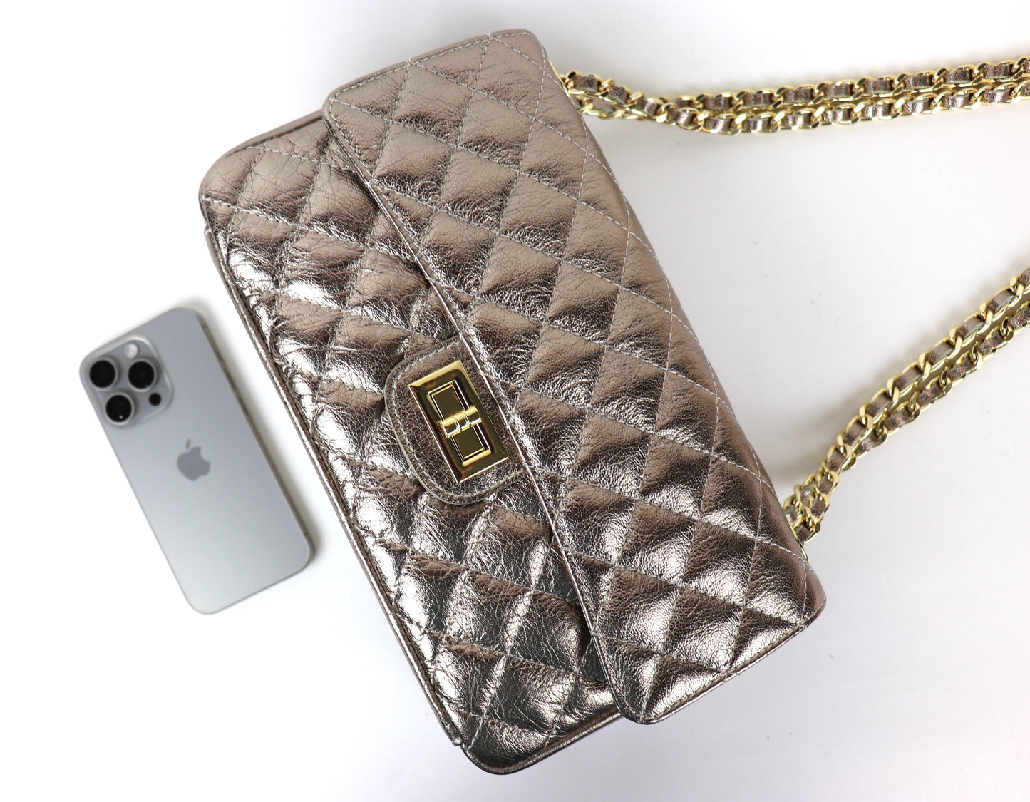 A bronze quilted leather bag with a gold twist-lock closure and chain strap, displayed next to a silver iPhone for size reference.