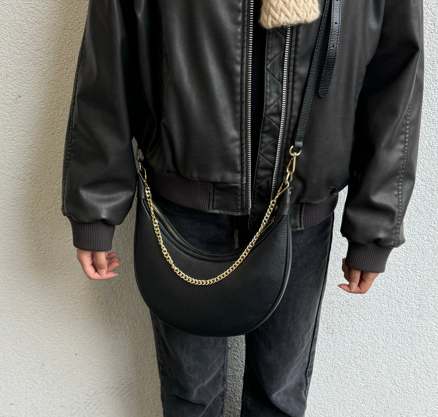 A person wearing the black leather crossbody bag with a gold chain strap, seen from a front angle.