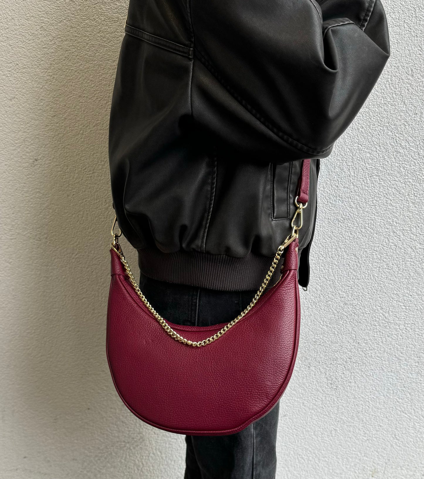 A person wearing the burgundy leather crossbody bag with a gold chain, pictured from a side angle.