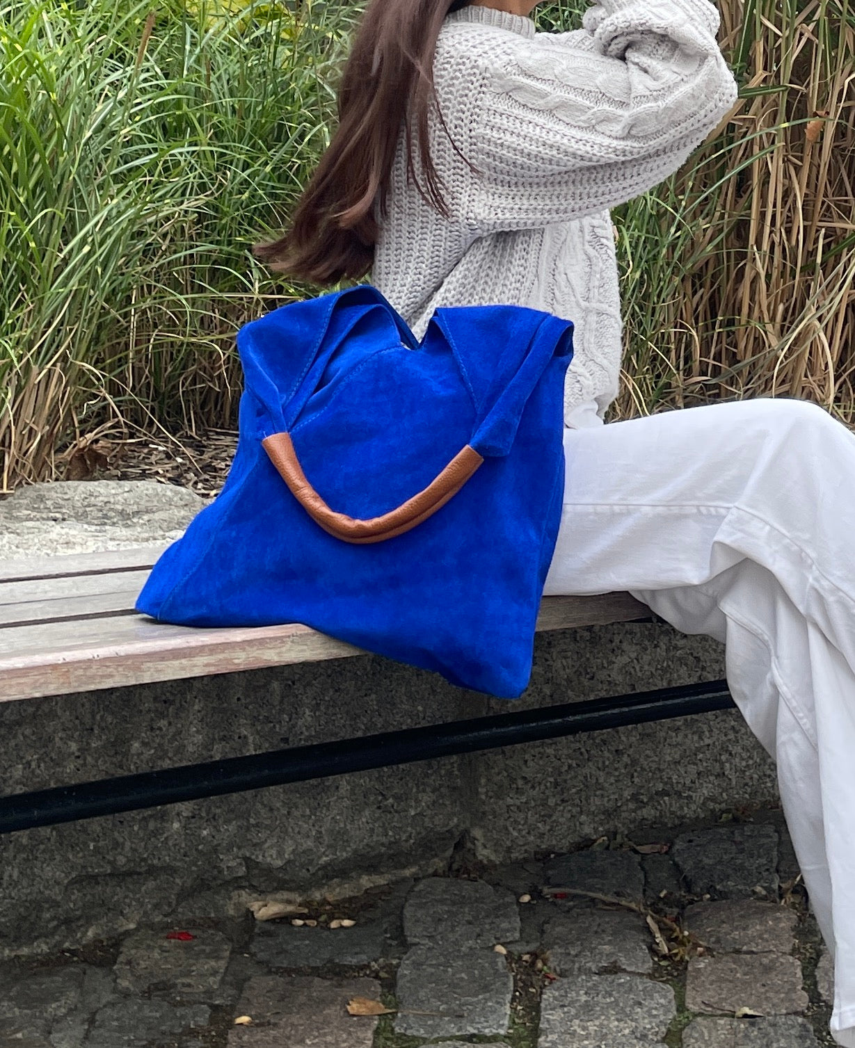 Model sitting on a bench with the Royal Blue Samantha Large Tote Laptop Bag resting beside them, wearing a cozy sweater and white pants, outdoors in a natural setting.