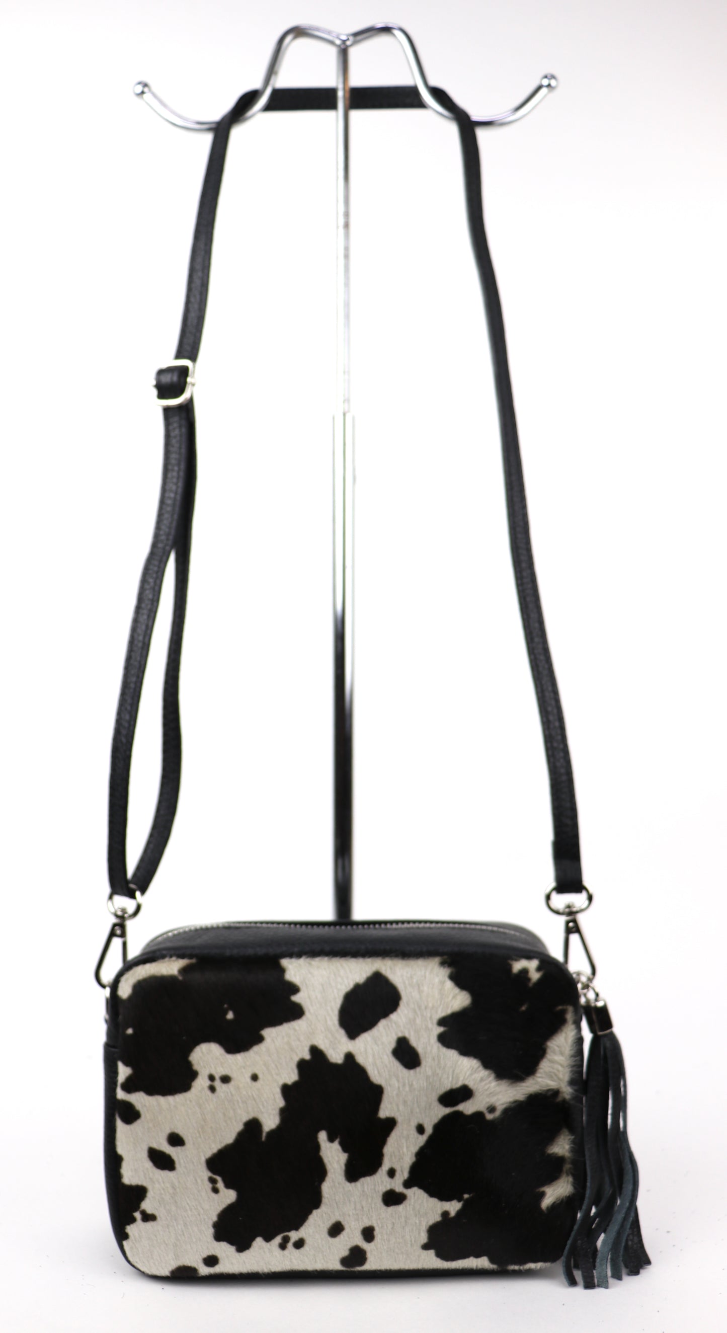 Cow print leather bag with a long strap, displayed hanging against a white background.