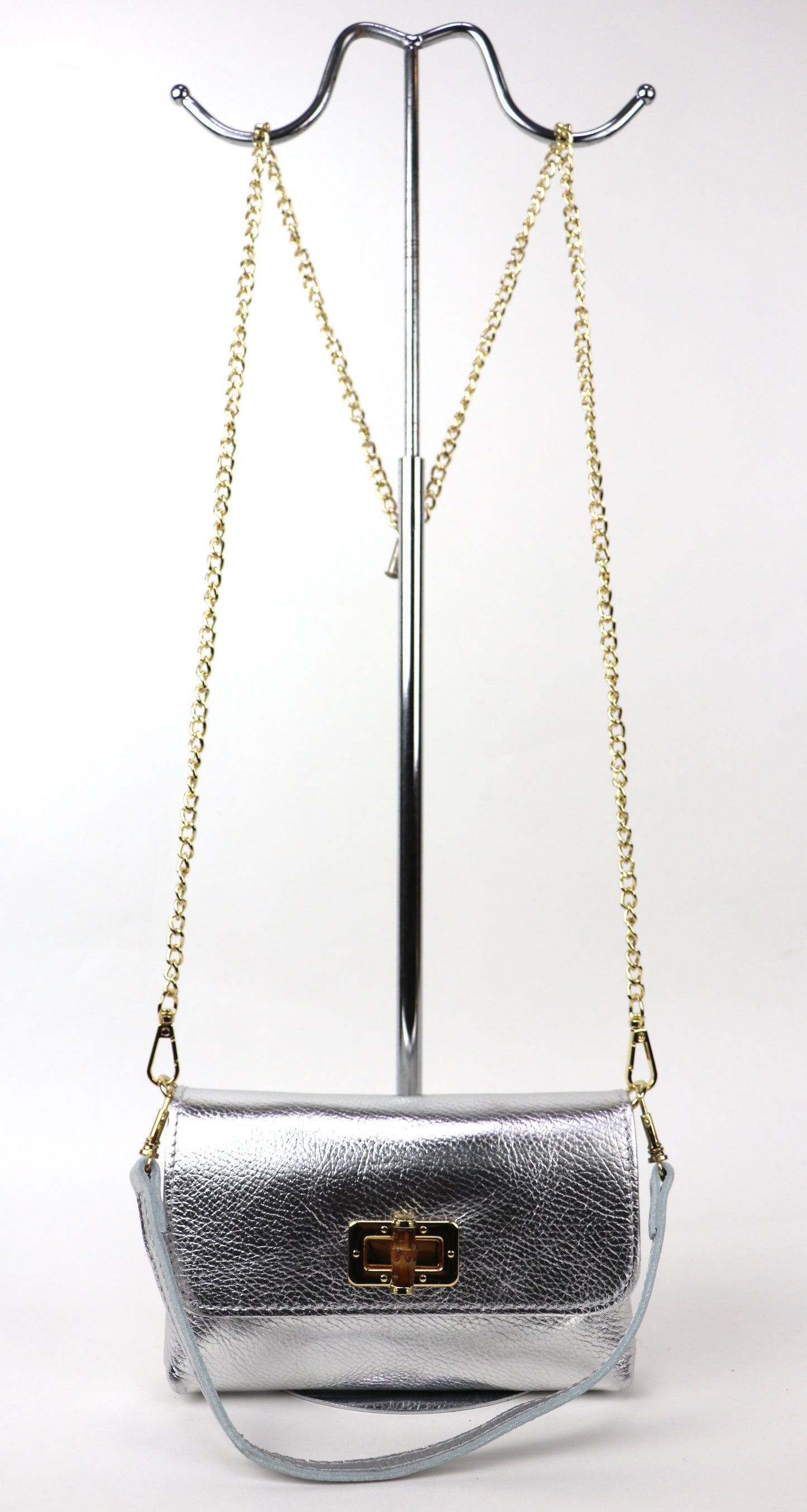 Silver metallic leather bag hanging from a gold chain, showing its overall shape.
