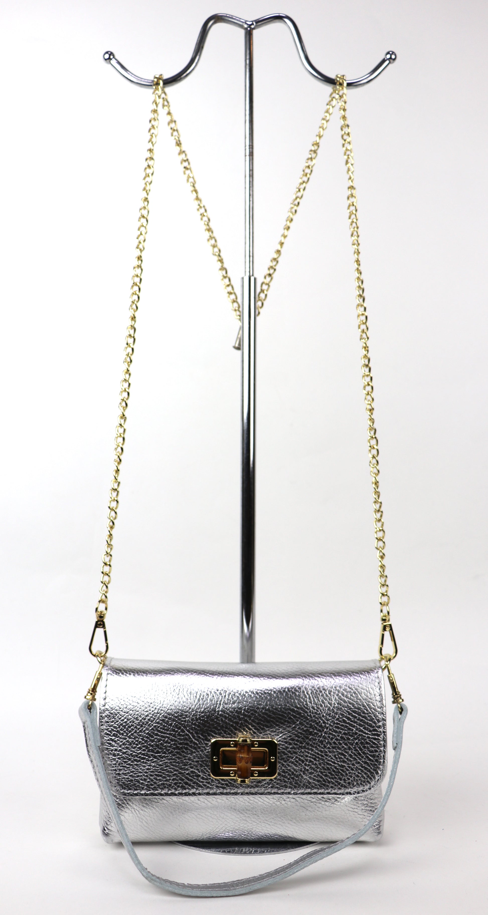 Silver metallic leather bag hanging from a gold chain, showing its overall shape.
