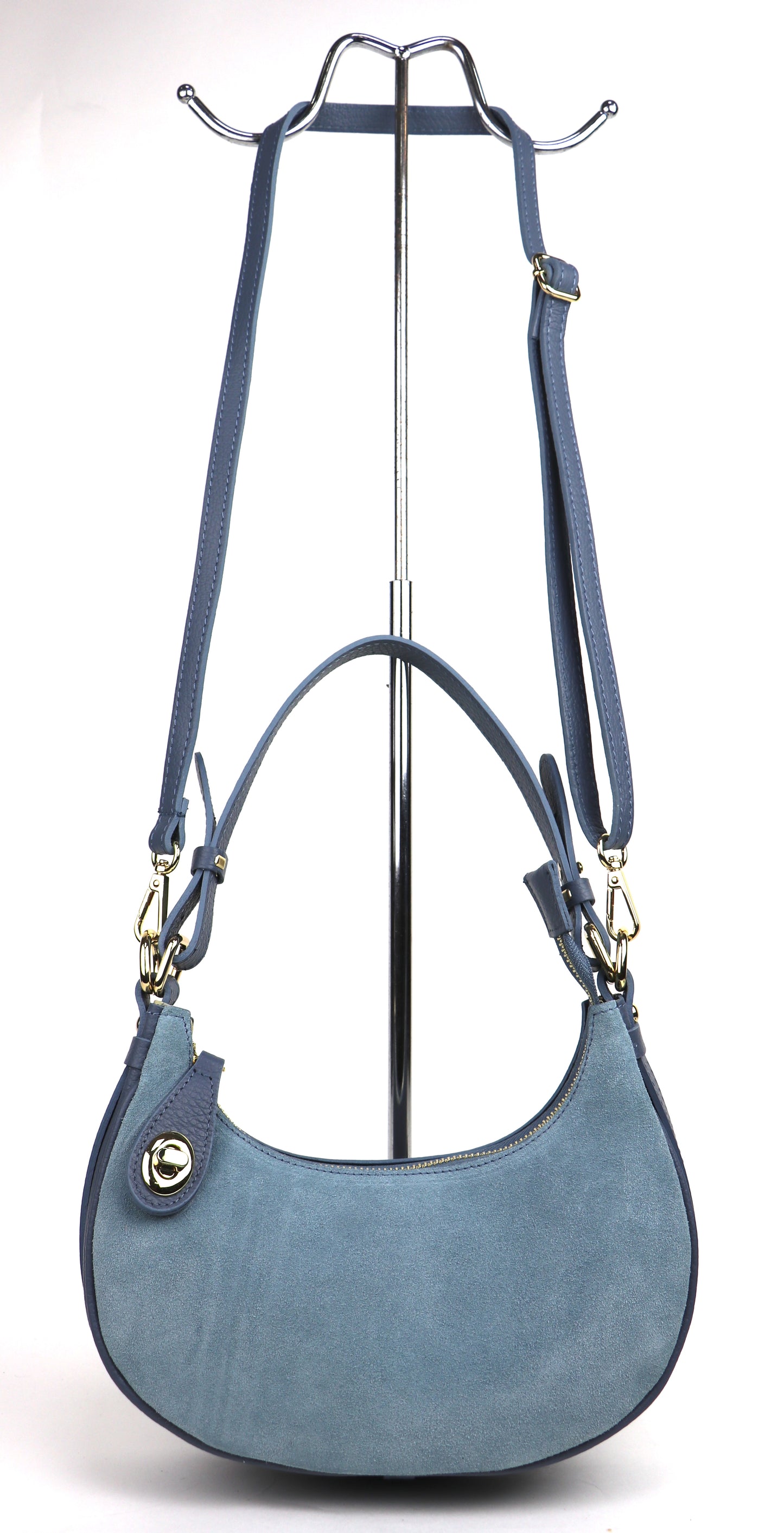 Denim Blue small half moon shoulder/crossbody bag displayed on a metal stand, showing the front view with gold-tone hardware, suede texture, and adjustable strap.

