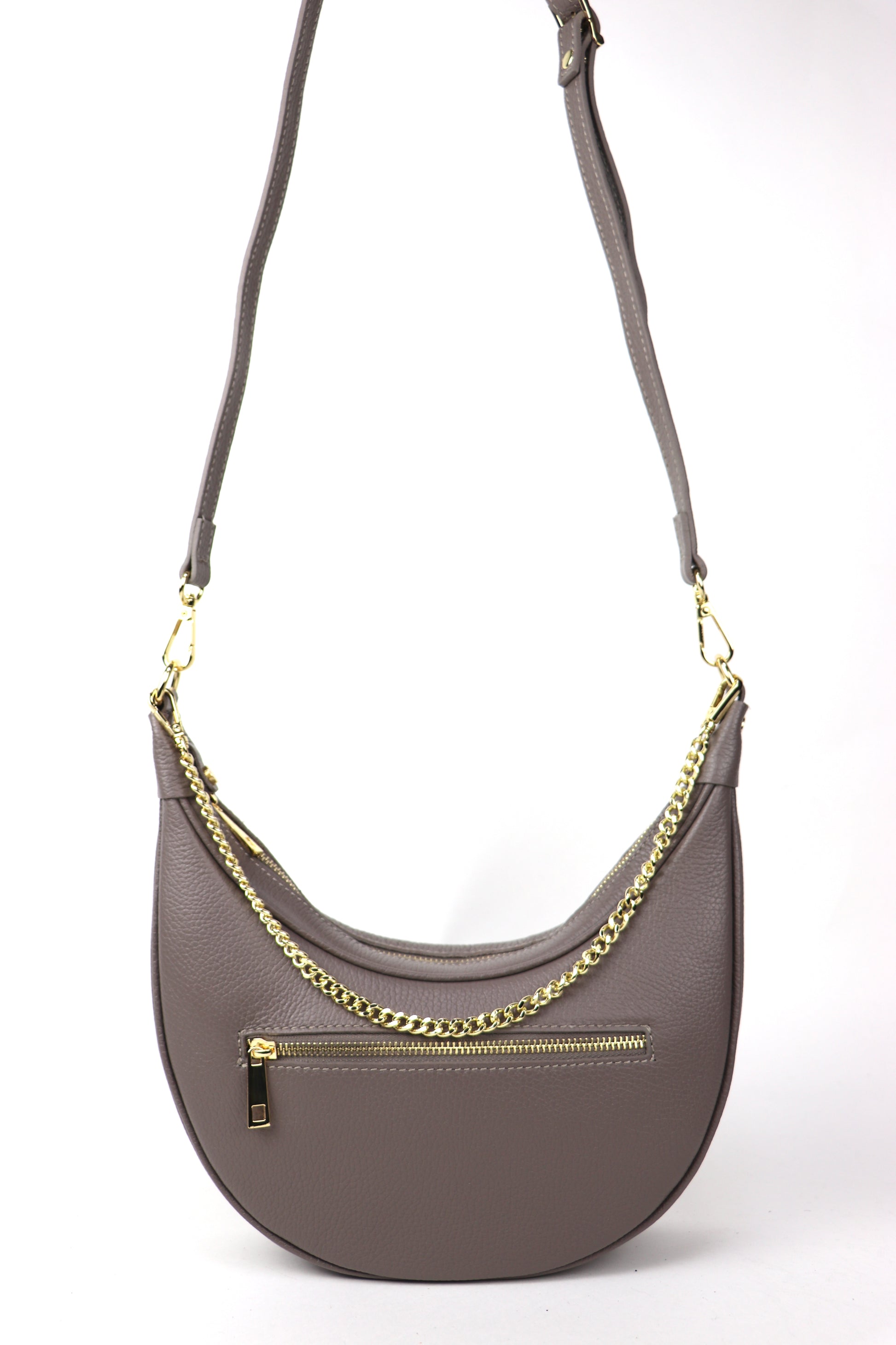 A taupe crescent-shaped leather crossbody bag with a gold chain strap, shown from the front. The bag has a gold zipper pocket on the front, photographed against a white background.