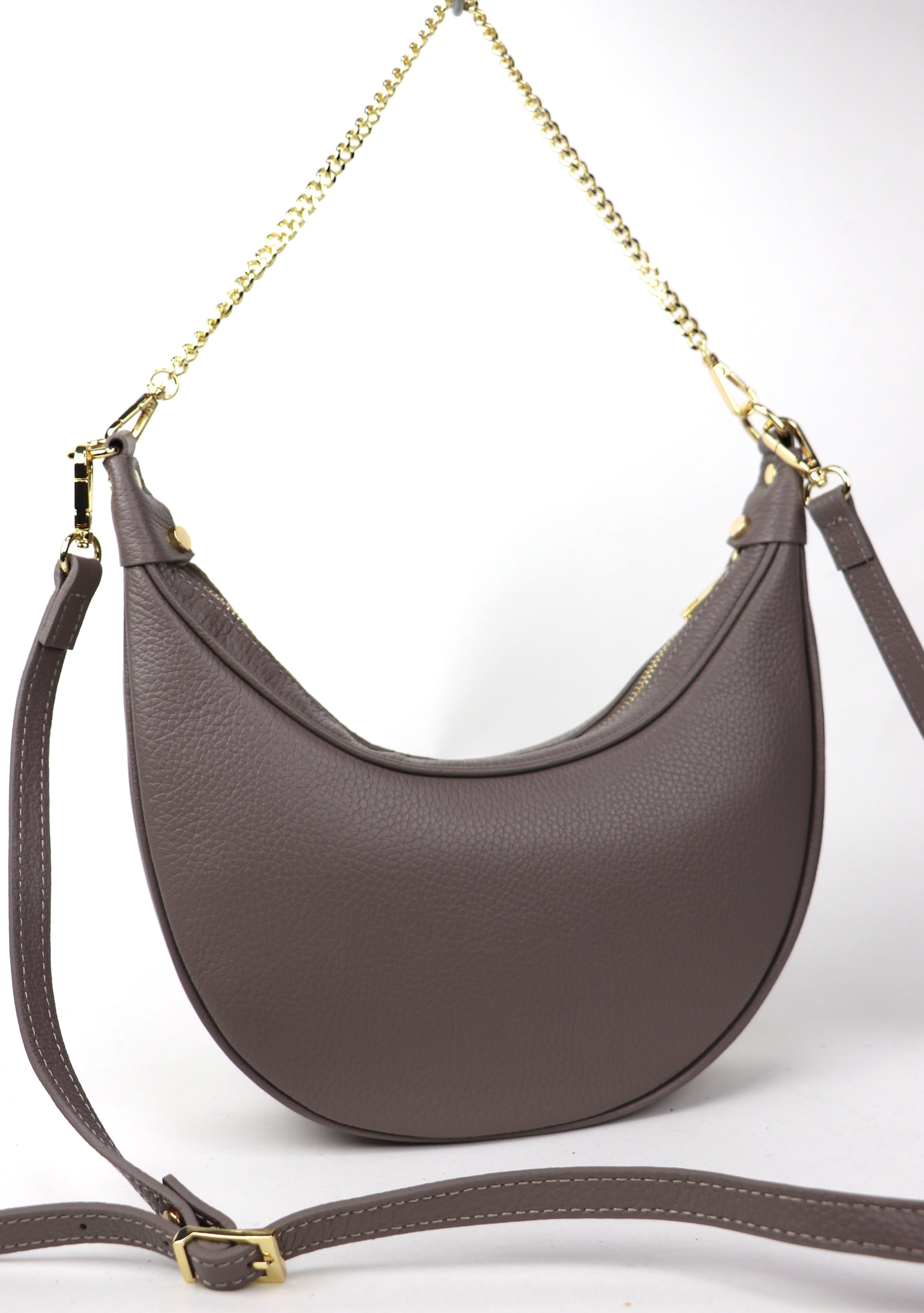 A taupe crescent-shaped leather crossbody bag with a gold chain strap, shown from the back, emphasizing the smooth leather texture and minimalist design.