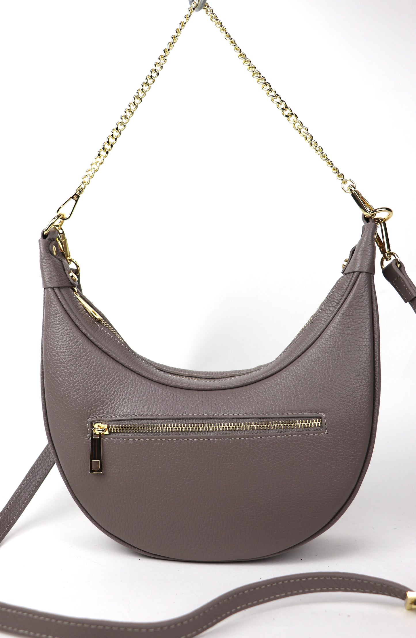 The taupe leather crossbody bag with a gold chain strap, shown from the back. It features a gold zipper pocket on the back for additional storage, displayed against a white background.