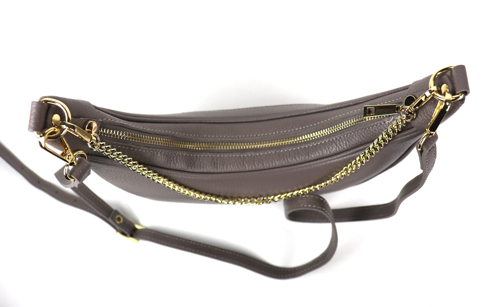 A taupe crescent-shaped leather crossbody bag shown from the top, with a partially open zipper, highlighting the gold hardware and textured leather. The adjustable leather strap is visible, resting beside the bag.