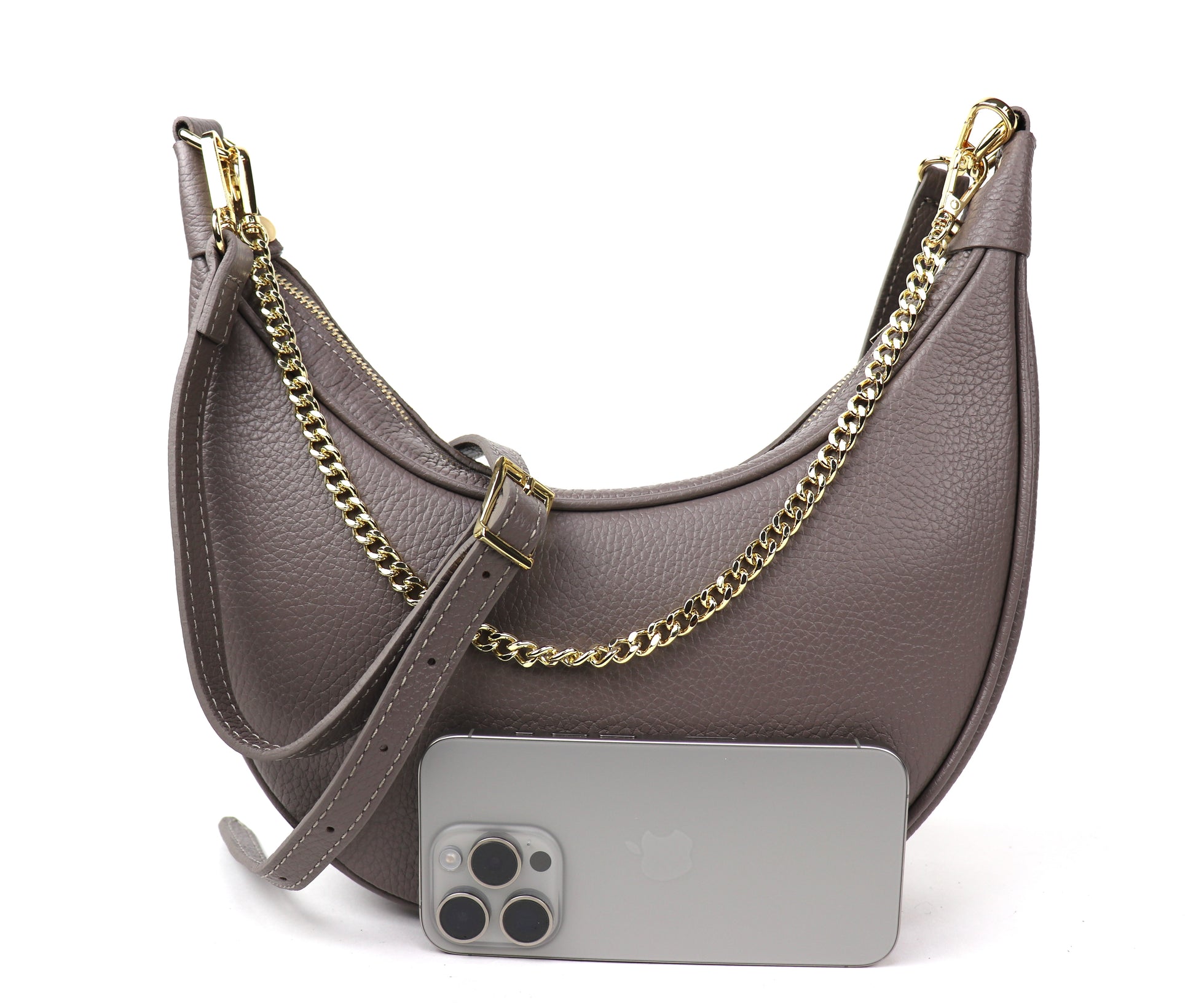 A taupe crescent-shaped leather crossbody bag with a gold chain strap, shown from the front. A silver smartphone is placed in front of the bag for size comparison, highlighting the bag’s sleek design and gold hardware.