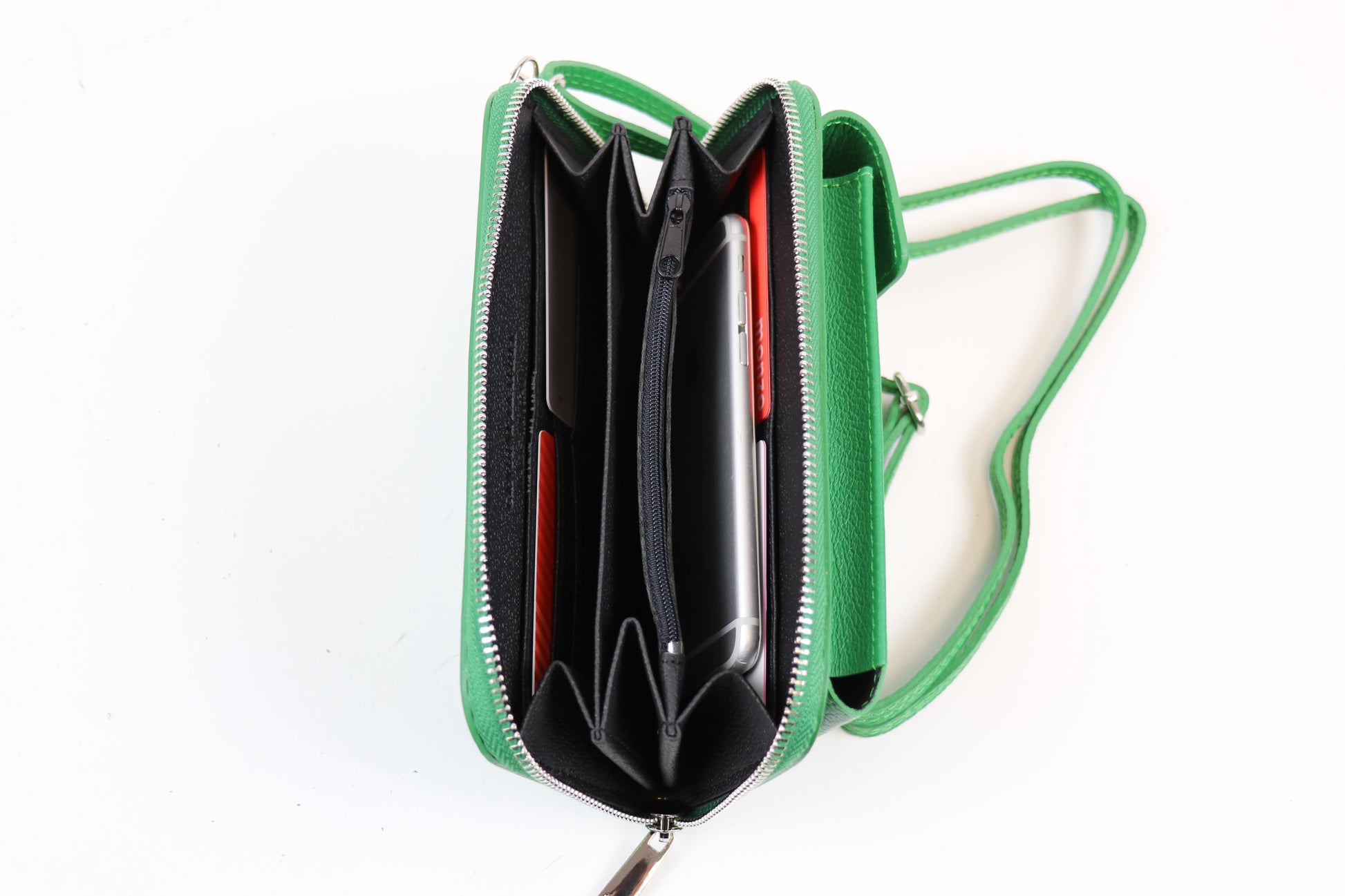 Open green crossbody bag displaying multiple compartments with a phone and cards stored inside, along with an attached green strap.






