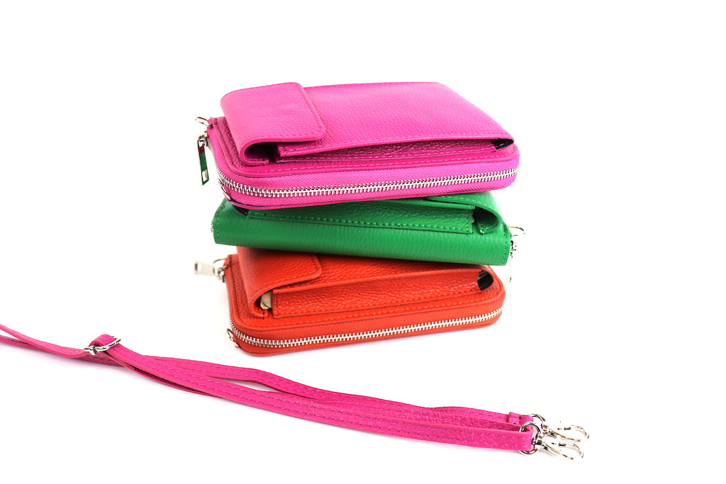 Stack of crossbody bags in pink, green, and orange with a detachable pink strap placed beside them.