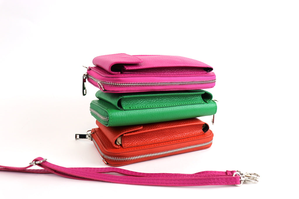 Stack of crossbody bags in pink, green, and orange with a detachable pink strap placed beside them.