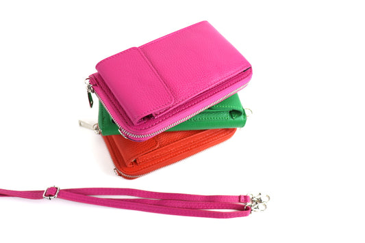 Stack of crossbody bags in pink, green, and orange with a detachable pink strap placed beside them.